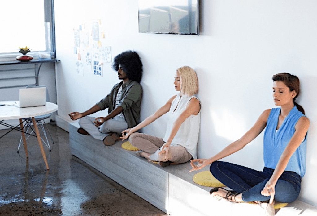 Three people sitting on a wall doing yoga.