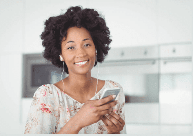 A woman holding her cell phone and wearing headphones.